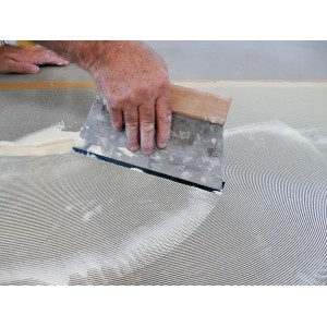 Auftragen von Soudal Vinyl- & PVC-Kleber mit Spachtel auf Boden.