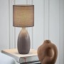 Graue PR Home Uno Tischleuchte mit geripptem Keramikfuß und Stoffschirm auf Büchern. Skandinavisches Design für Innenleuchten.