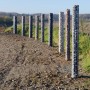 Reihe Gabionen-Säulen, eckig, feuerverzinkt, gefüllt mit Steinen in verschiedenen Farben.