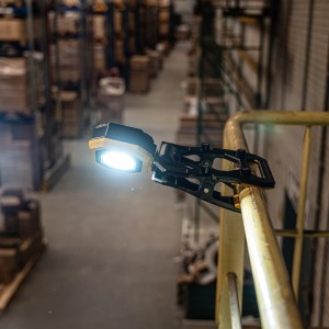 LED-Akku-Arbeitsleuchte mit Klemme an Geländer in Lagerhalle. Baustrahler mit Akku.