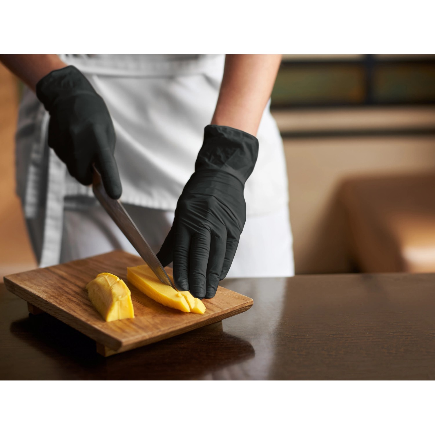 Schwarze Einmalhandschuhe (latexfrei, Gr. S) beim Schneiden von Käse.