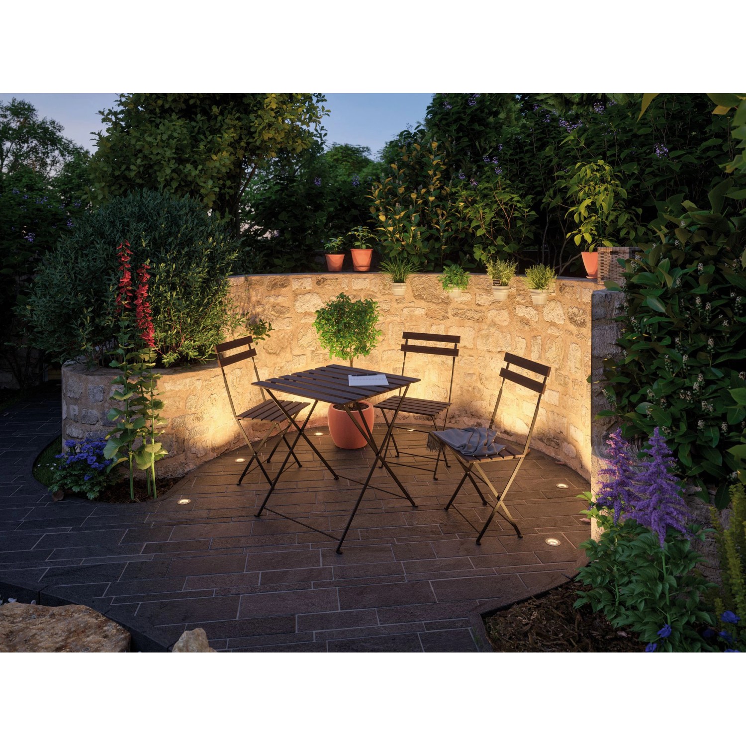 Paulmann Plug&Shine Bodeneinbaustrahler Set beleuchtet Garten mit Tisch und Stühlen warmweiß.