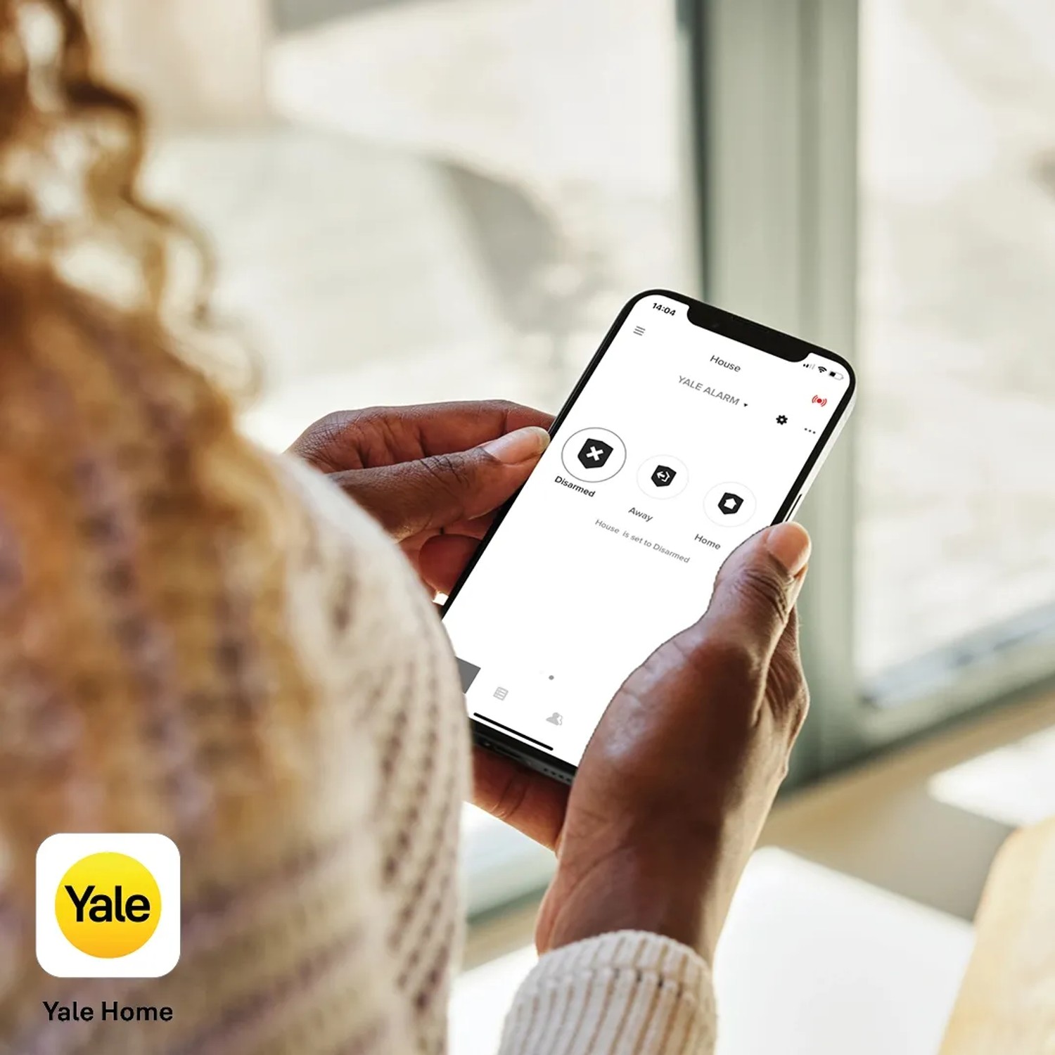 Frau bedient Yale Alarmanlage Smart Alarm Starterkit per App auf Smartphone.