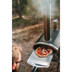 Ooni Pizzaschieber (40 cm) mit Pizza vor Pizzaofen. Grillutensil aus Edelstahl und Nylon.