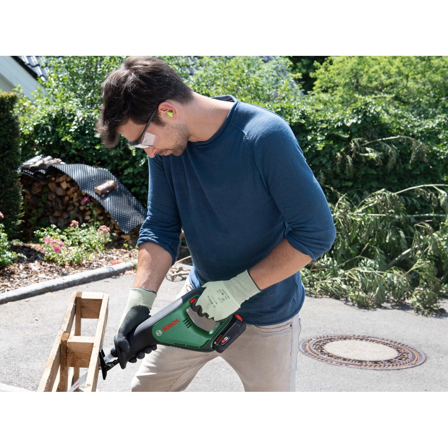 Mann sägt Holz mit Bosch 18 V Akku-Säbelsäge AdvancedRecip 18 im Garten.