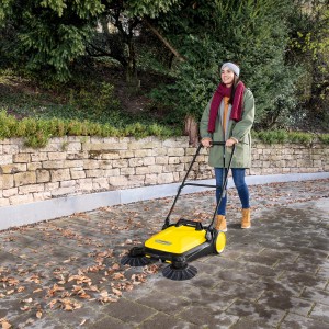 Frau kehrt Laub mit gelber Kärcher Kehrmaschine S 4. Zubehör: Seitenbesen (2 Stk.) für feuchtes Kehrgut.