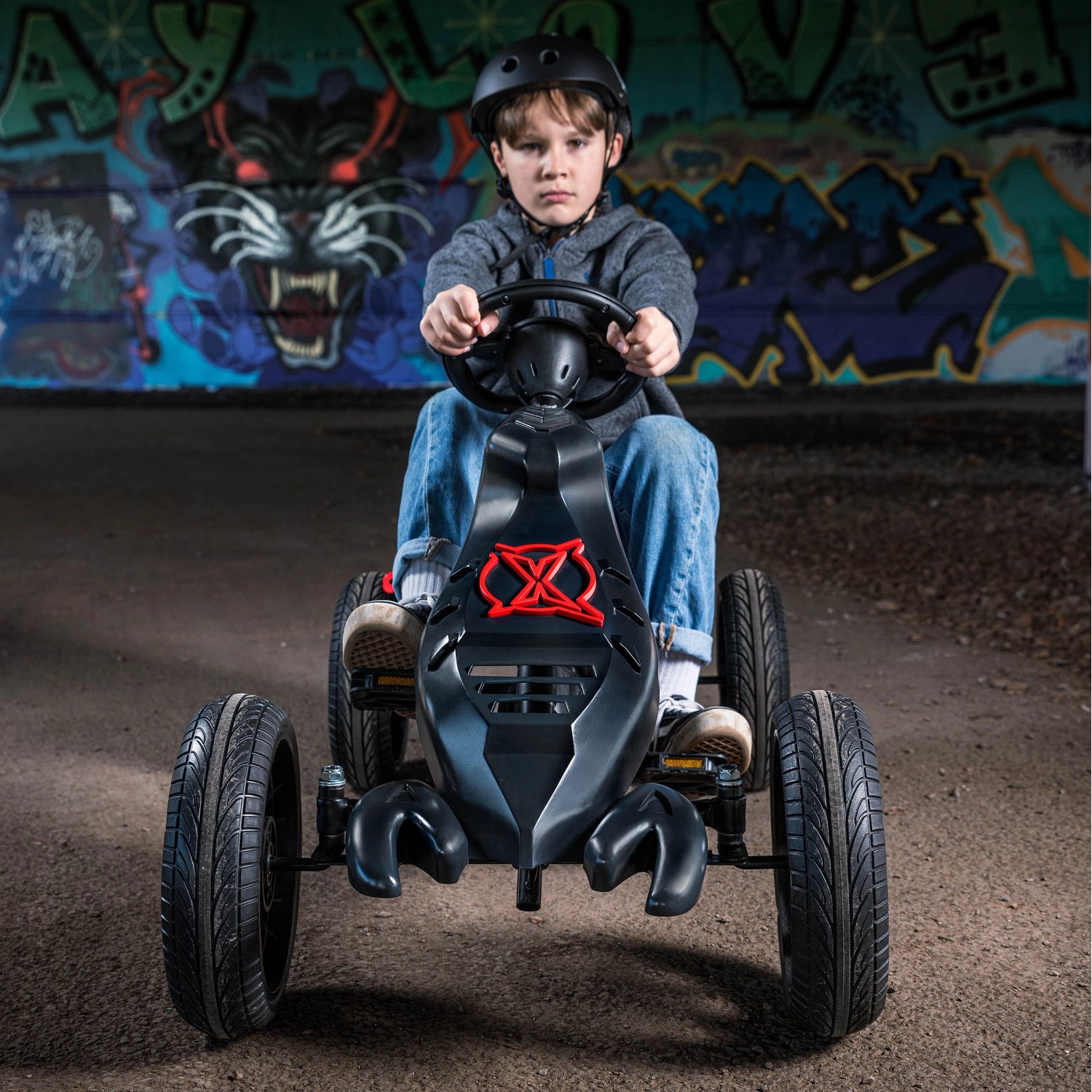 Schwarzes Xootz Go-Kart Venom mit Kind auf Betonuntergrund vor Graffitiwand.