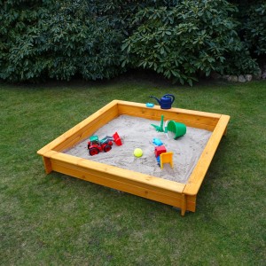 Quadratischer Sandkasten Tessa 140x140 cm aus Holz mit Spielzeug im Garten.