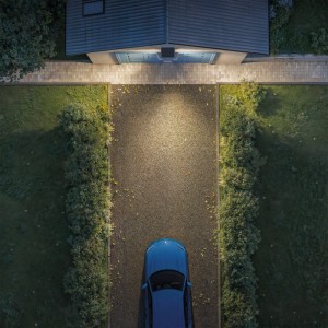 Philips Solar-LED-Außenstrahler Zyren beleuchtet Hofeinfahrt mit Auto und Haus im Hintergrund.