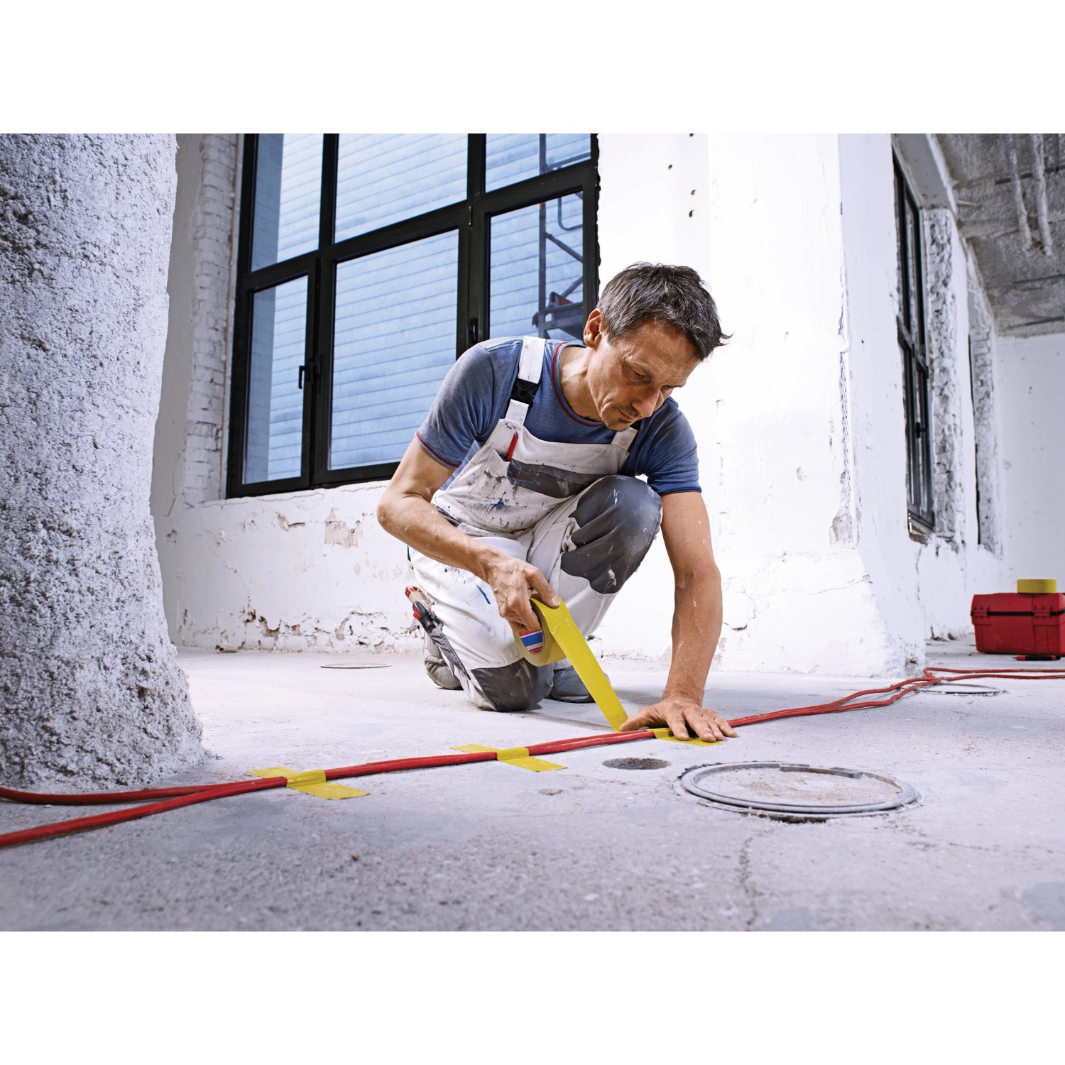 Handwerker fixiert Kabel mit gelbem Tesa Betonband Gewebeklebeband auf dem Boden.