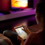 Frau steuert Philips Hue Lightstrip Plus mit Tablet, indirekte Beleuchtung im Hintergrund.
