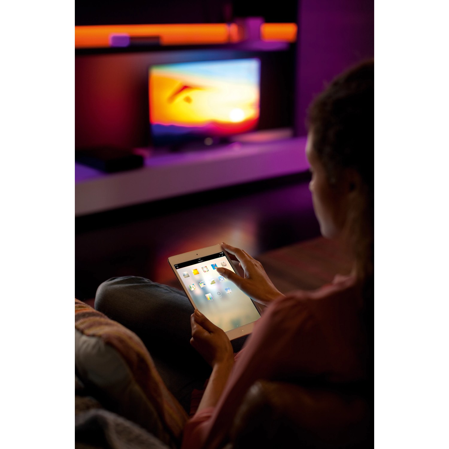 Frau steuert Philips Hue Lightstrip Plus mit Tablet, indirekte Beleuchtung im Hintergrund.