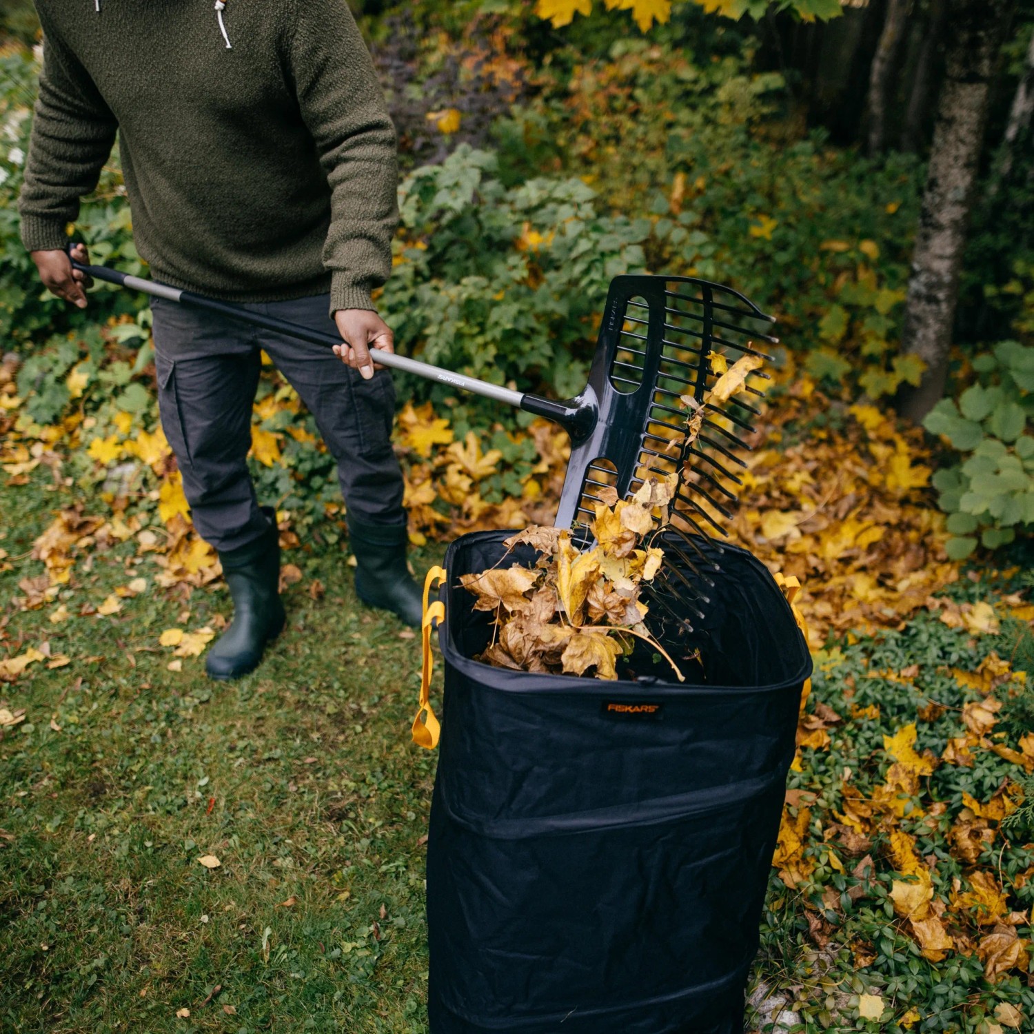 Mann befüllt Laubsack mit Fiskars Ergonomic Schaufelrechen. Besen & Rechen für Gartenarbeit.
