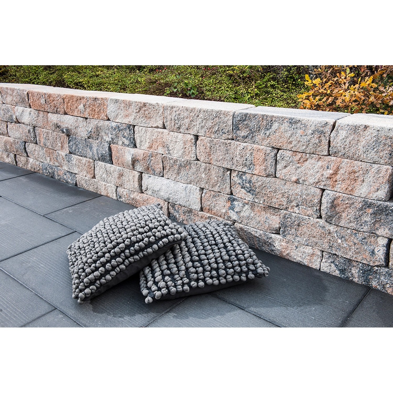 Diephaus Mauerstein Maximo Brista Muschelkalk als Gartenmauer, kombiniert mit grauen Kissen.
