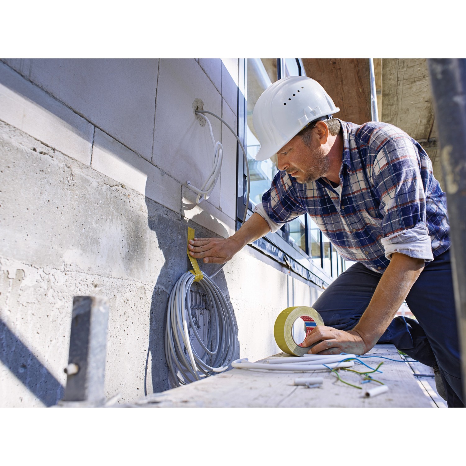 Handwerker fixiert Kabel mit gelbem Tesa Betonband Gewebeklebeband an einer Betonwand.