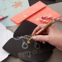 Hand schreibt "Merry Christmas" mit goldenem Edding Paintmarker E-750 auf schwarze Karte.