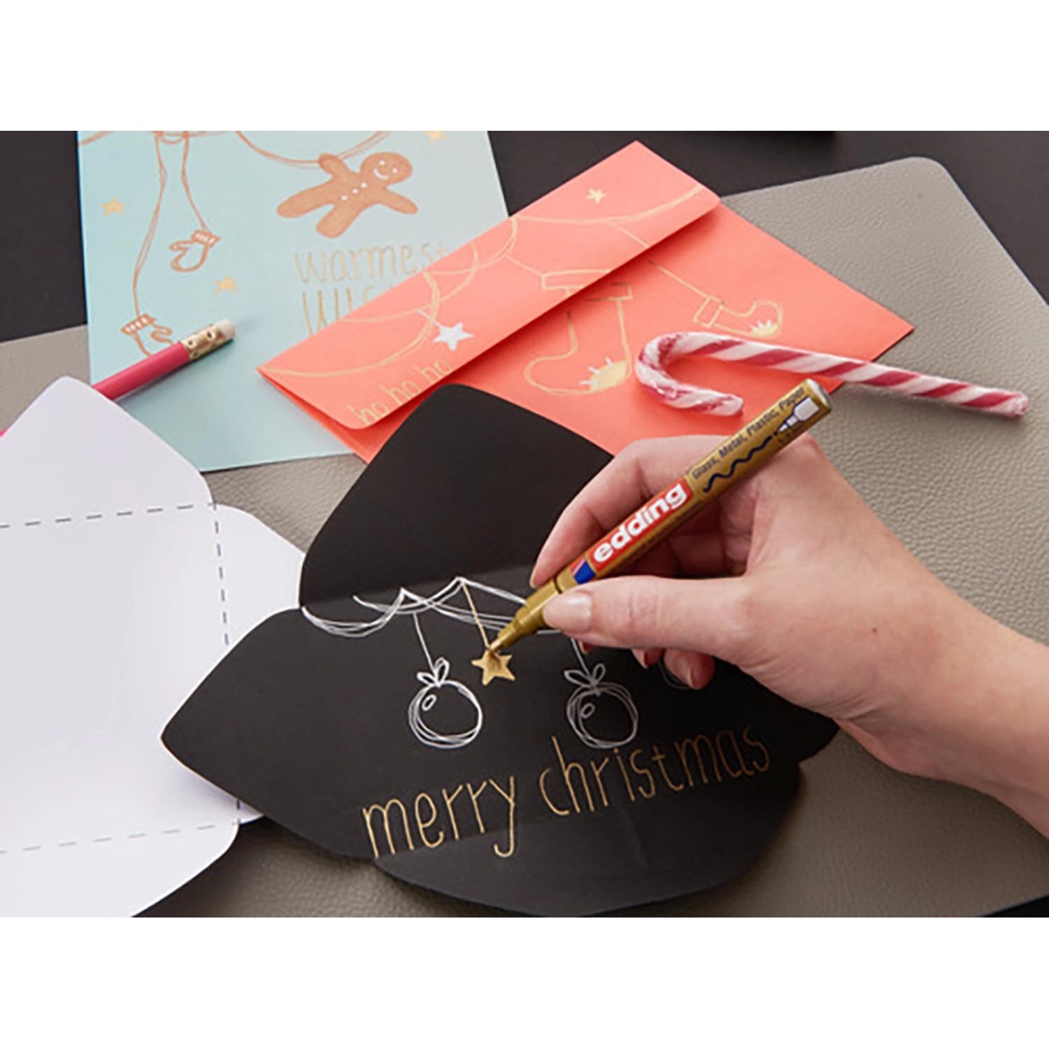 Hand schreibt "Merry Christmas" mit goldenem Edding Paintmarker E-750 auf schwarze Karte.