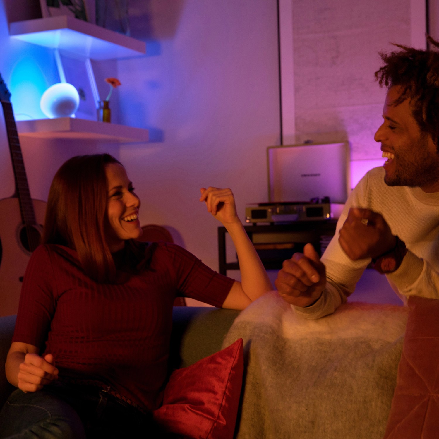 Paar entspannt mit Philips Hue Go LED Tischlampe, die farbiges Licht spendet.