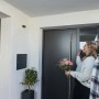 Abus Akku-Kamera Pro mit Basisstation in Weiß, montiert über einer Haustür, mit Personen davor.