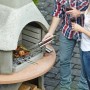 Buschbeck Grillkamin Carmen Grau-Terrakotta beim Grillen mit Paar im Garten.