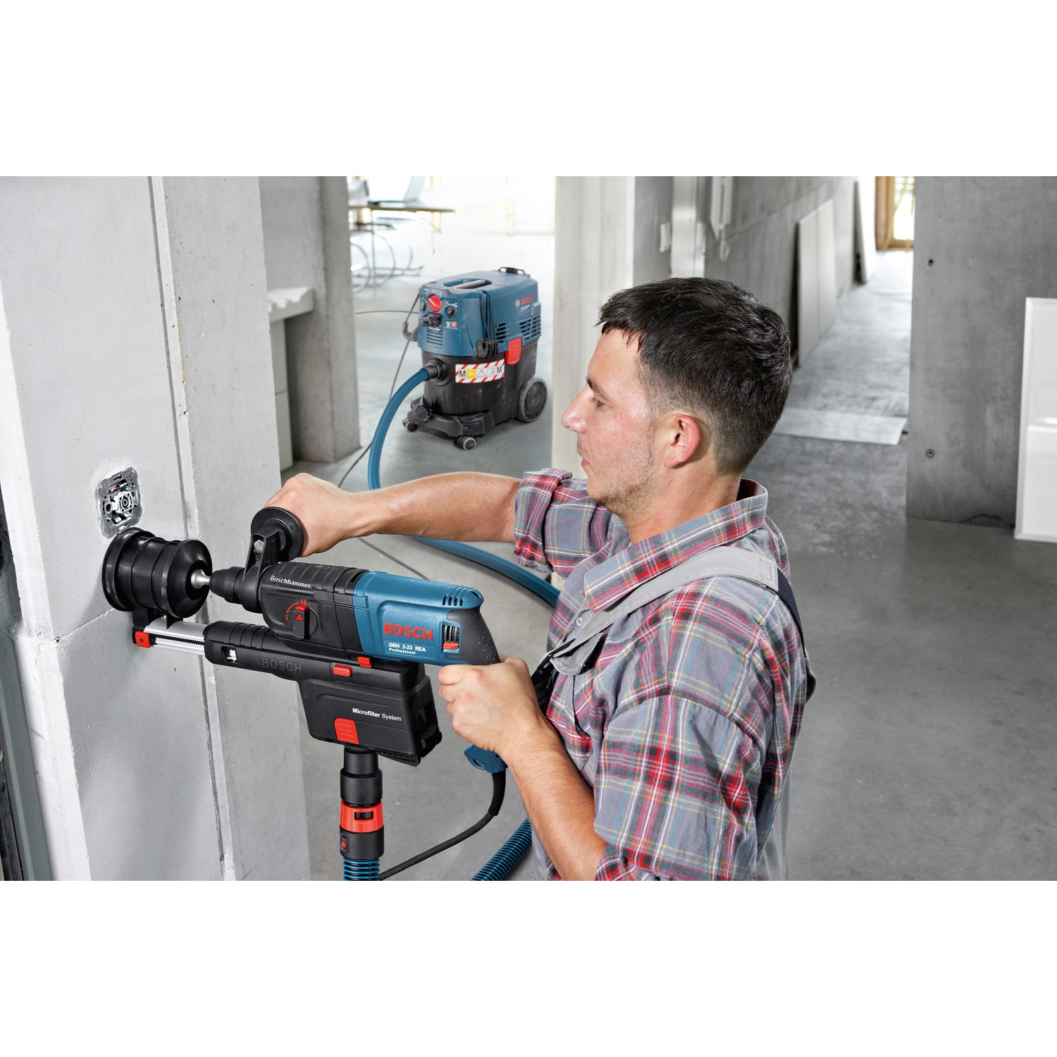 Handwerker bohrt mit Bosch Professional Bohrhammer, Staub wird vom Industriestaubsauger abgesaugt.