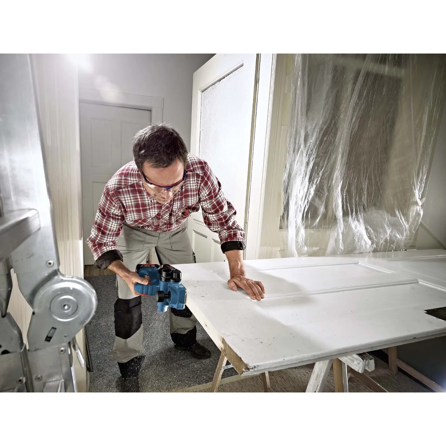 Handwerker hobelt mit dem Bosch Professional Akku-Hobel GHO 18V-LI Solo eine weiße Tür.