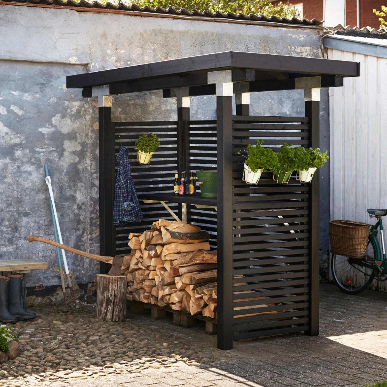 Schwarzer Sichtschutzzaun Tokyo aus Nadelholz, 180x180 cm, mit Holzstapel und Gartenzubehör.