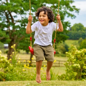 Kind schwingt auf roter Zwerkules Schaukel im Garten. Spielhaus Zubehör.