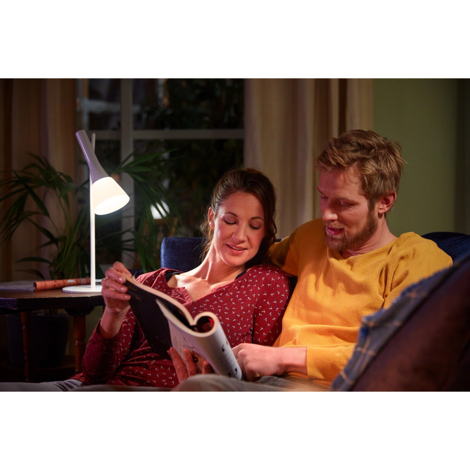 Paar liest bei Licht der Philips Hue White E14 LED-Lampe. Smarte Beleuchtung für gemütliche Stunden.