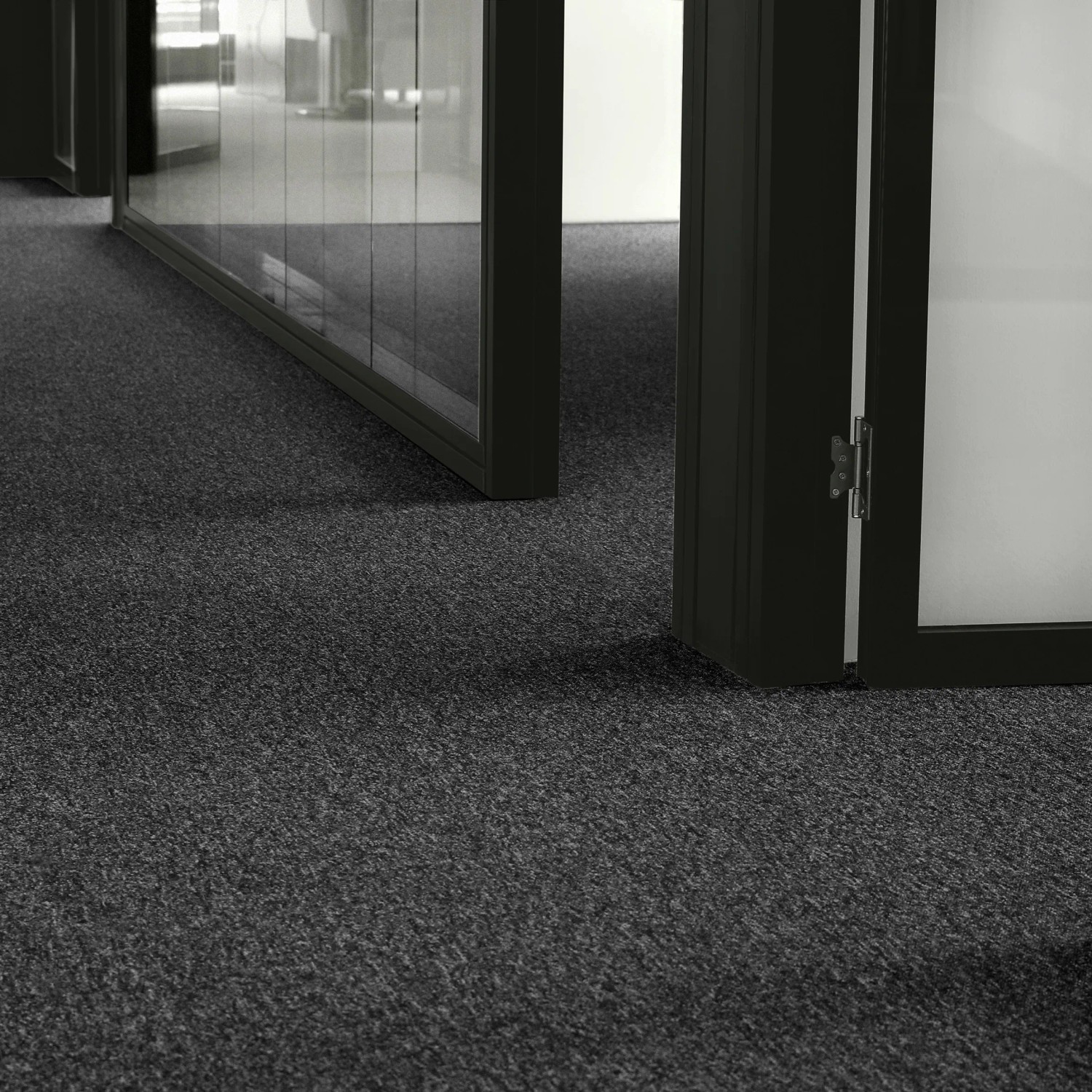 Anthrazitfarbener Andiamo Teppichboden Alvar Vlies als Meterware in einem Raum mit Glastüren.