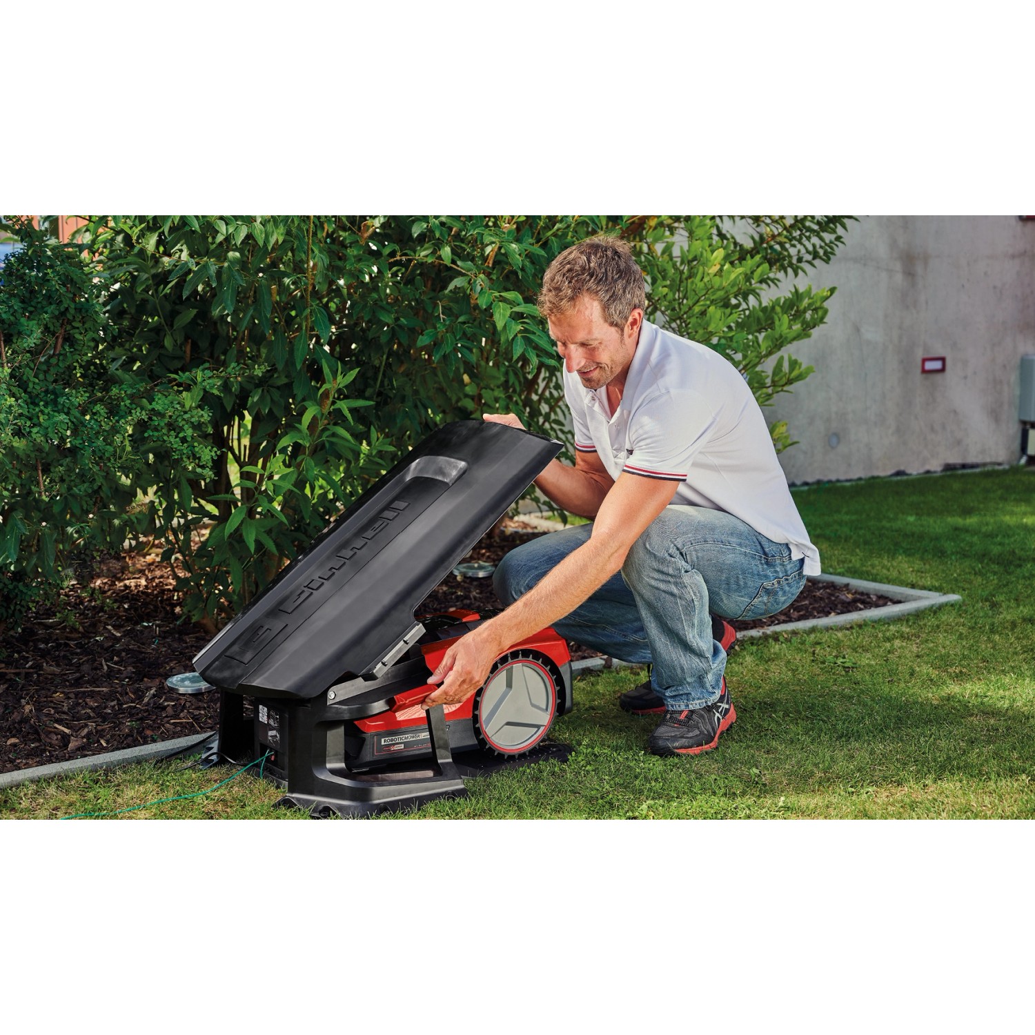 Einhell Mähroboter mit geöffneter Garage im Garten, bedient von einem Mann.
