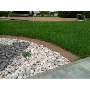 Braune Mähkante aus Beton zwischen Rasen und Kiesbeet zur Gartengestaltung.