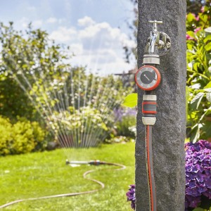 Gardena Bewässerungsuhr am Wasserhahn mit Rasensprenger im Garten.
