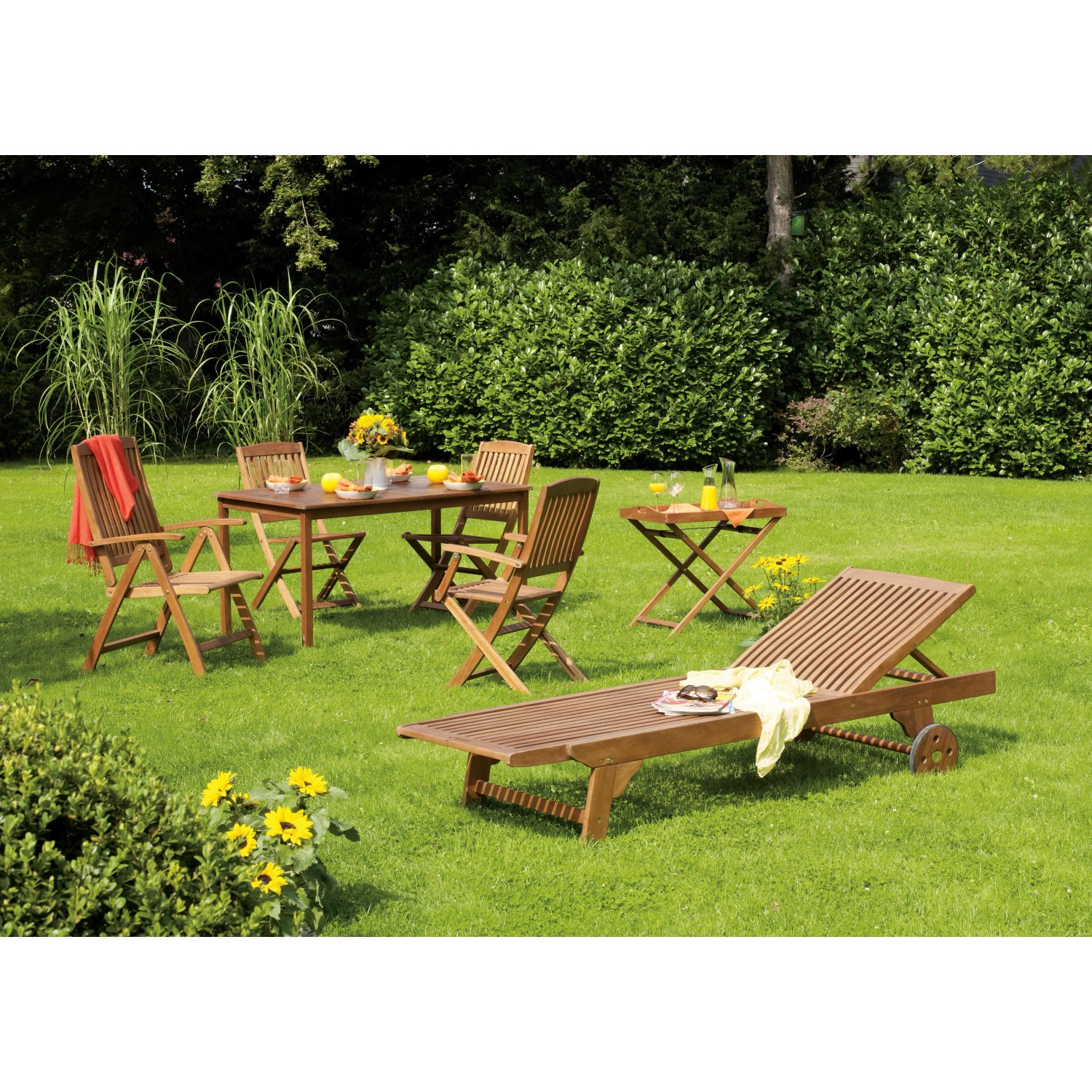Gartenmöbel-Set Greenville aus Holz mit Klappsessel, Tisch, Liege und Serviertablett auf einer grünen Wiese.