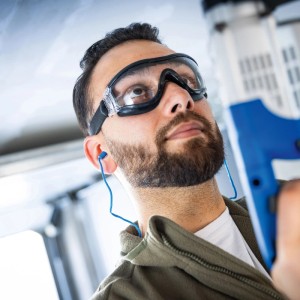 Mann mit LUX-TOOLS Gehörschutzstöpseln mit Band (Blau) und Schutzbrille bei der Arbeit.