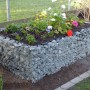 Eckiges Gabiona Gabionen-Hochbeet (40x100x40cm) mit Steinfüllung und bunten Blumen bepflanzt.