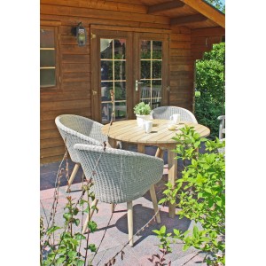 Runder Gartentisch Arvada Natur Ø 110 cm mit Stühlen auf Terrasse vor Holzhütte.