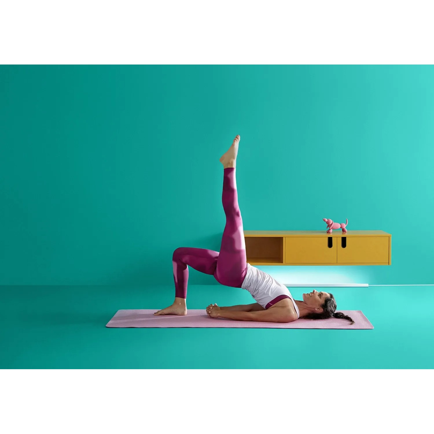 Frau macht Yoga mit WiZ LED Stehleuchte im Hintergrund, die farbiges Licht an die Wand wirft.