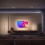 Weiße Philips Hue Gradient Signe Tischleuchte im Wohnzimmer mit TV und Sofa.