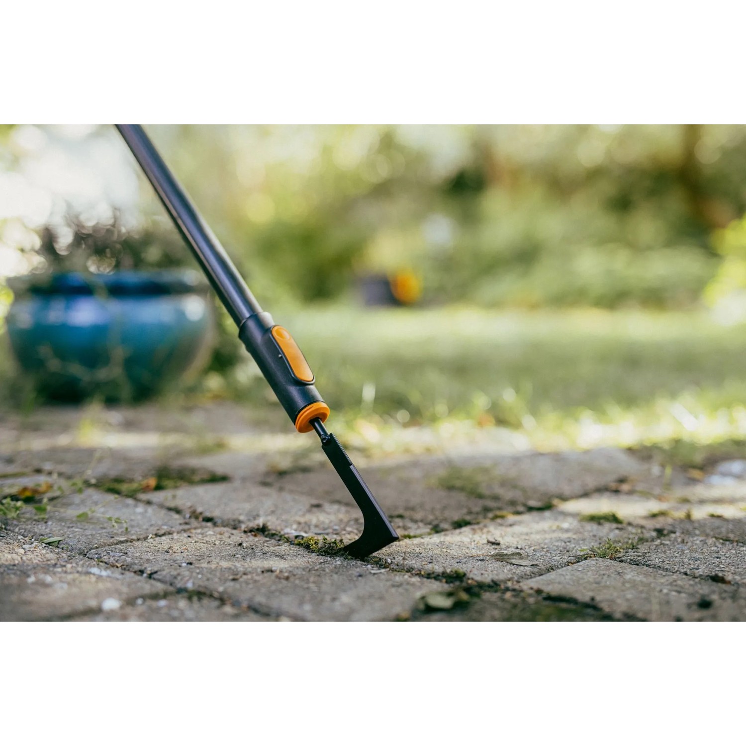Fiskars OneClick Fugenkratzer in Aktion: Unkrautentfernung zwischen Pflastersteinen.