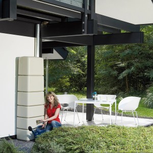 4rain Slim Regenwassertank 650 l sandbeige mit Zubehör. Frau befüllt Gießkanne.