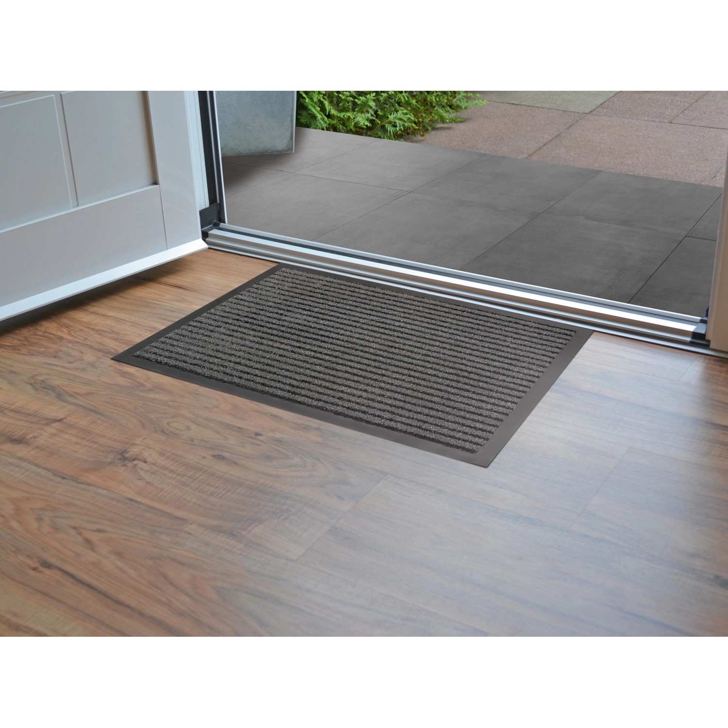 Anthrazitfarbene Sauberlaufmatte Stirling 80x120 cm vor einer Tür. Fußmatte mit Streifenmuster für den Innenbereich.