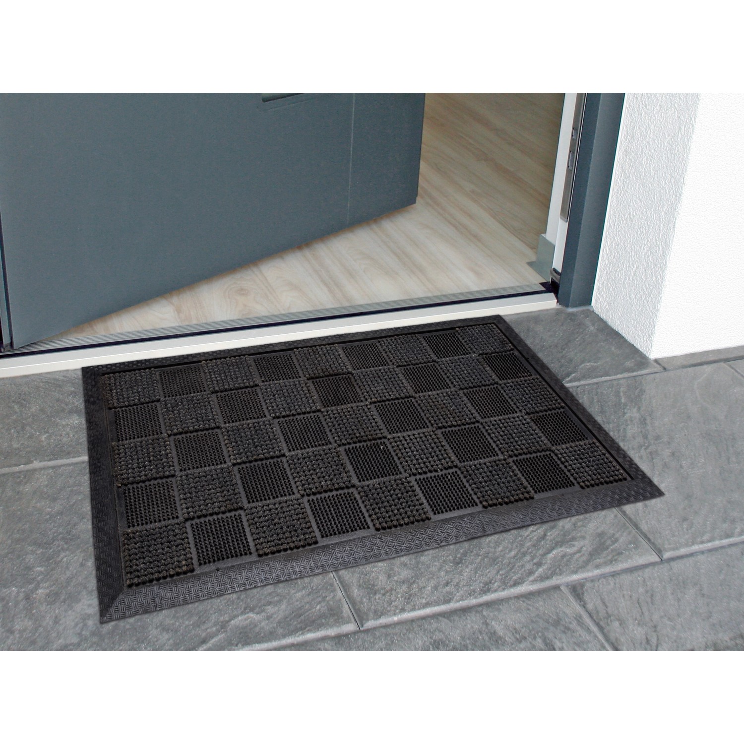 Schwarze Gummipinmatte 40x70 cm mit Beflockung vor einer Tür, ideal für den Außenbereich.