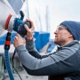 Mann schleift Boot mit Bosch Professional Exzenterschleifer GEX 40-150. Blaue Schleifmaschine mit Schleifteller und Absaugung.