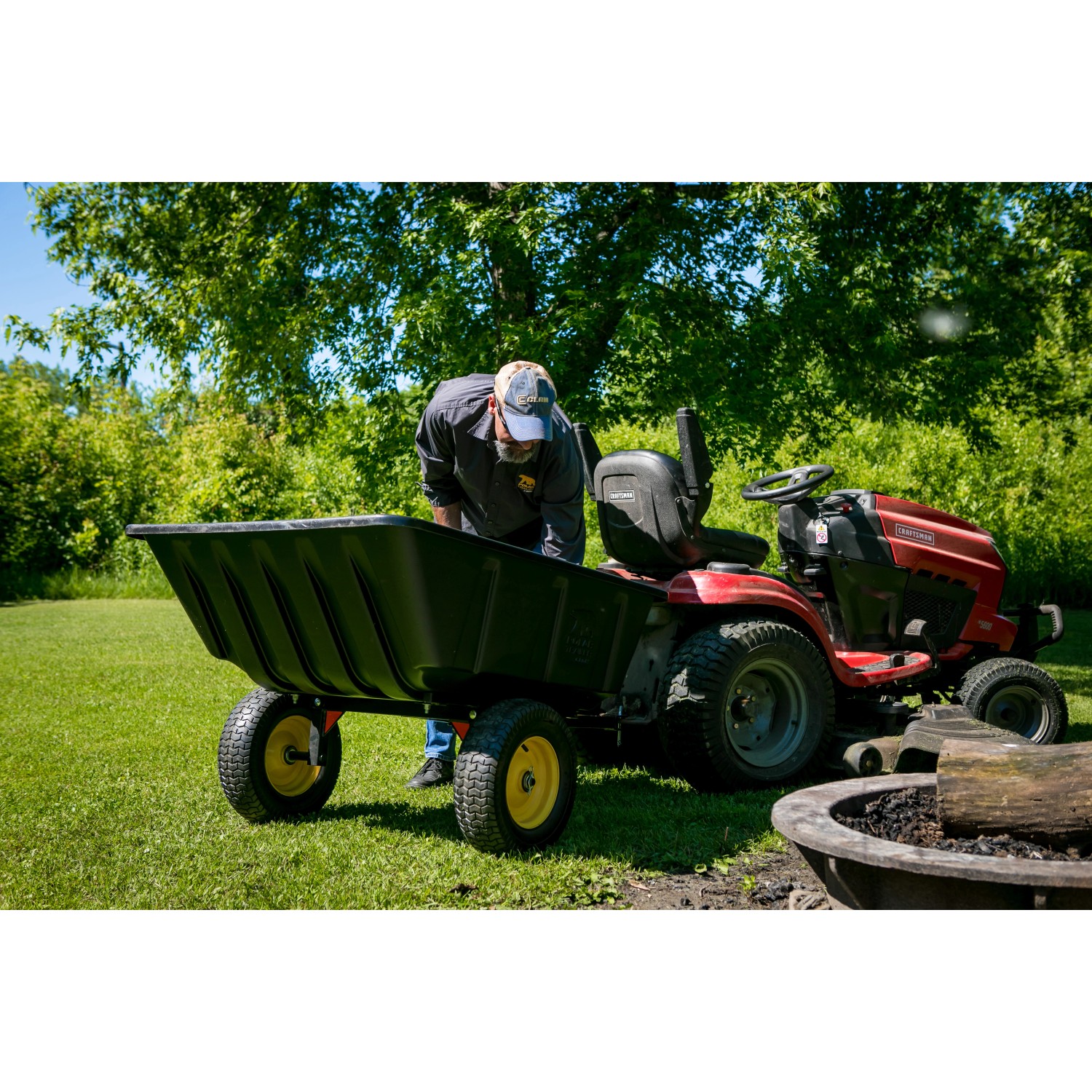 Polar Anhänger Schubkarre LG900, schwarz, mit Kippfunktion und Traktor im Garten.