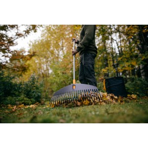 Fiskars Ergonomic Laubbesen L im Einsatz: Person harkt Laub im Garten mit dem breiten Rechen.