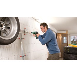 Mann bohrt mit Bosch Akku-Bohrhammer Uneo Maxx in Wand. Reifenhalterung sichtbar.