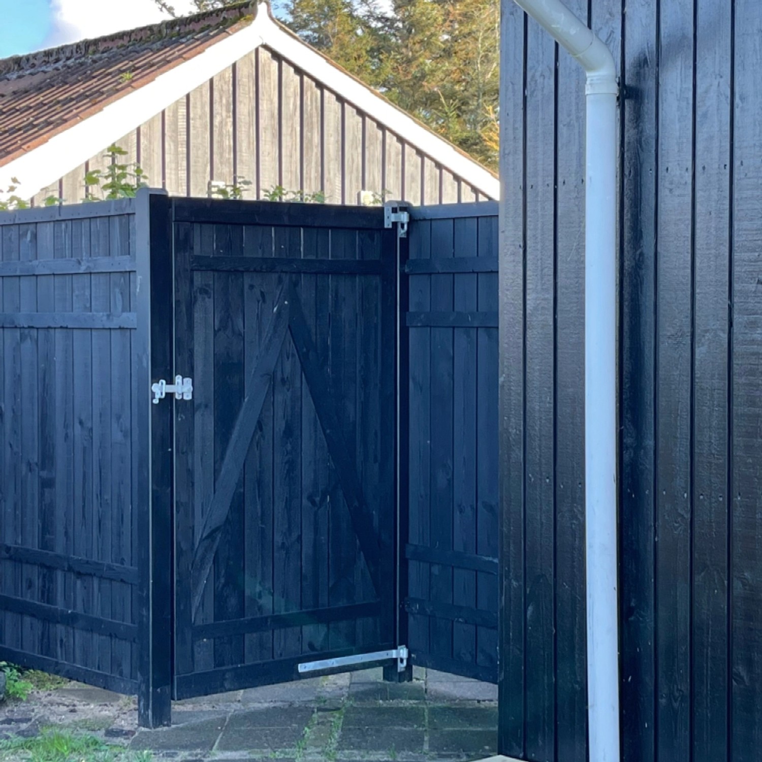 Schwarzer Sichtschutzzaun Rustik aus Nadelholz, 180x180 cm, mit geöffneter Tür.