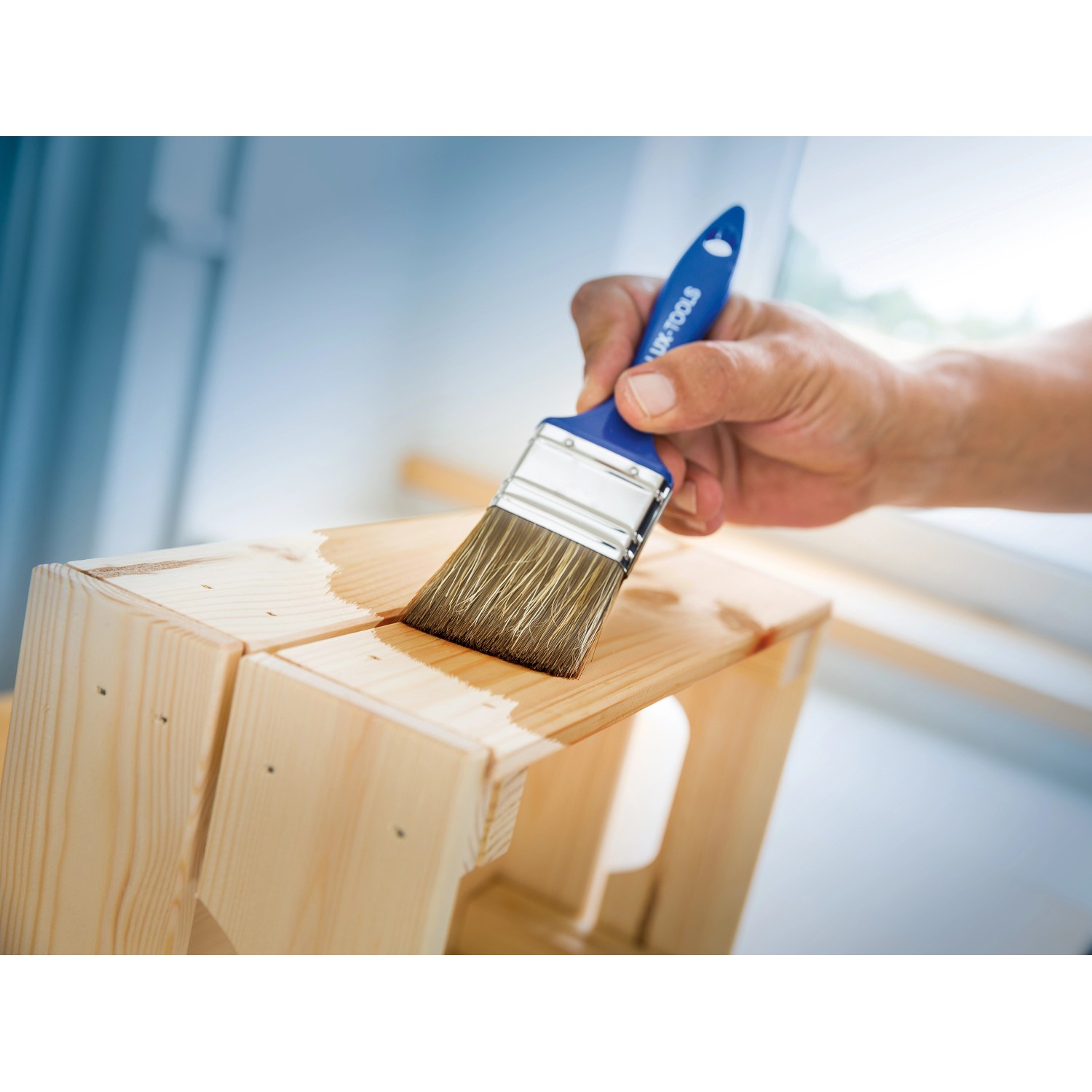 LUX Flachpinsel 70mm beim Lasieren von Holz. Pinsel mit blauem Griff.