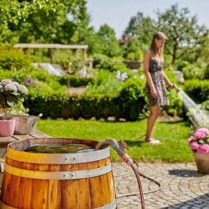 Gardena Regenfasspumpe 4700/2 Inox im Einsatz: Frau bewässert Garten mit Pumpe aus Holzfass.